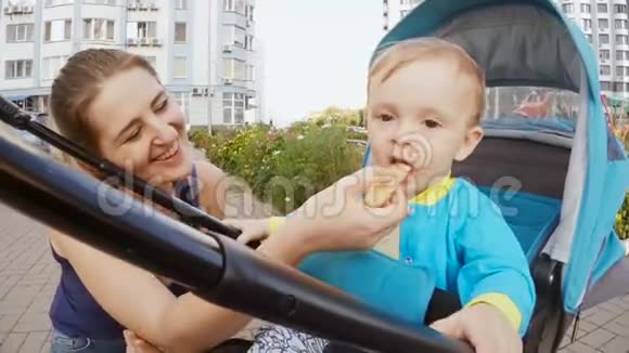 快乐的微笑母亲喂养她的小儿子坐在婴儿车上视频的预览图