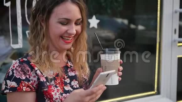 白人迷人的年轻卷发女人在智能手机上写短信手里拿着咖啡慢动作视频的预览图