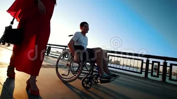 在夏日的夜晚带着病腿的男人在轮椅上与女友在水边散步视频的预览图