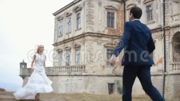 快乐的年轻新婚夫妇朝前奔跑坠入彼此的怀抱宏伟的中世纪城堡背景视频的预览图