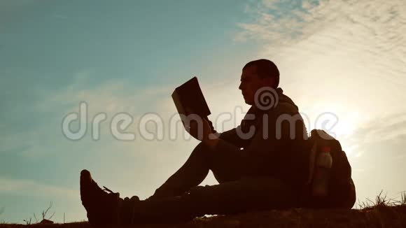 男学生在公园里背着背包看日落在天空生活方式日落时的人读书剪影视频的预览图