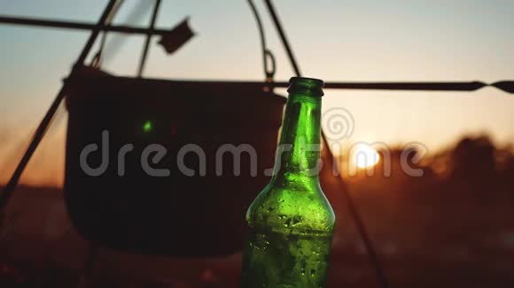 点燃一个大锅篝火一瓶啤酒在日落剪影露营特写旅游户外休闲旅游视频的预览图