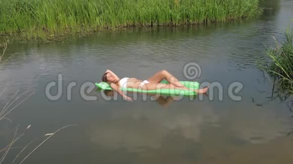 穿着白色泳装沐浴在水中床垫上的年轻女子视频的预览图