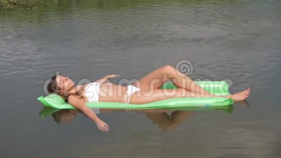 穿着白色泳装沐浴在水中床垫上的贴身年轻女子视频的预览图