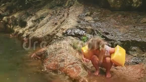 手挽手的小女孩坐在河边吃的湿石头上视频的预览图