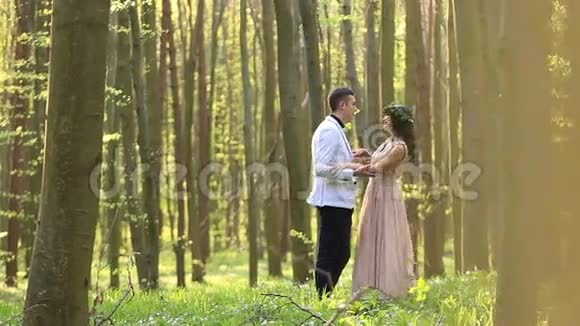 春天阳光明媚的森林里年轻美丽的新婚夫妇边走边亲吻视频的预览图