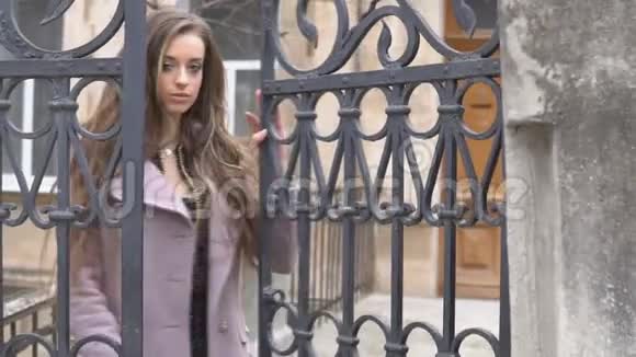 穿外套的女孩在街边的栅栏后面摆姿势视频的预览图