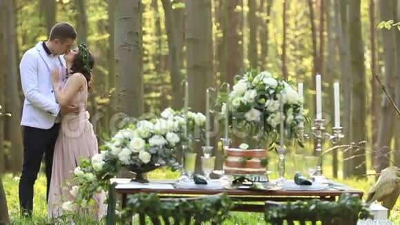 在绿色的春天森林为相爱的情侣布置浪漫晚餐美丽的新郎新娘亲吻视频的预览图