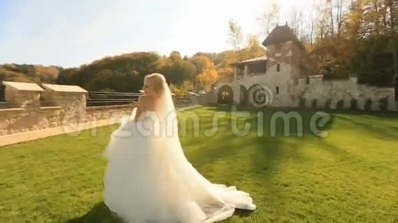 穿着白色裙子的漂亮金发新娘在中世纪城堡庭院的镜头前摆姿势视频的预览图