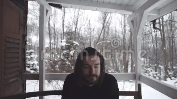 一位身穿黑色毛衣的英俊青年坐在一个古老的木制门廊上视频的预览图