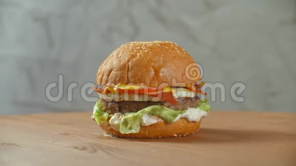 带有牛肉西红柿蘑菇和黄瓜的大汉堡和融化的奶酪在木板上轻轻旋转视频的预览图