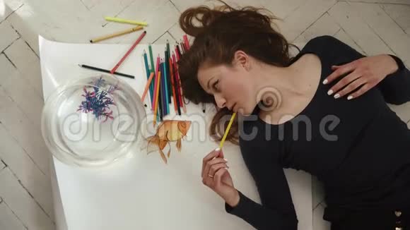 可爱的年轻女艺术家在白色背景上拍摄一张小金鱼的照片顶部视图视频的预览图