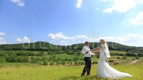 美丽的新娘和新郎走在绿色的田野上微笑着美丽的春景视频的预览图