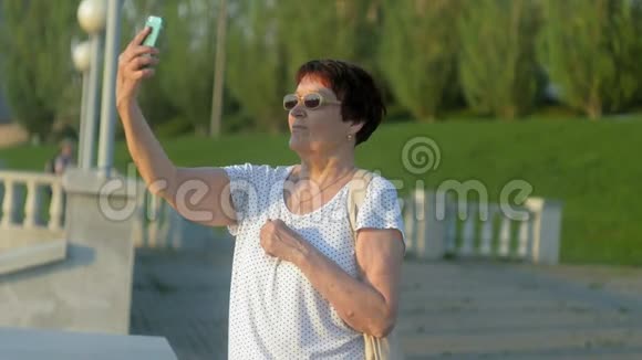 微笑的老妇人在公园打电话留言使用无线互联网连接智能手机的高级女性视频的预览图