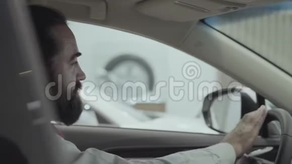 这幅画很吸引人有自信留着胡子的商人坐在车里检查从车里买的新车视频的预览图