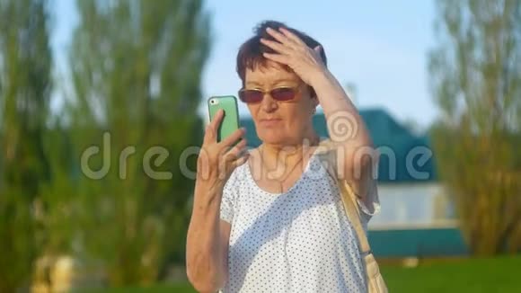 微笑的老妇人在公园打电话留言使用无线互联网连接智能手机的高级女性视频的预览图