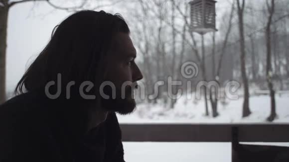 一位身穿黑色毛衣的英俊青年坐在一个古老的木制门廊上视频的预览图