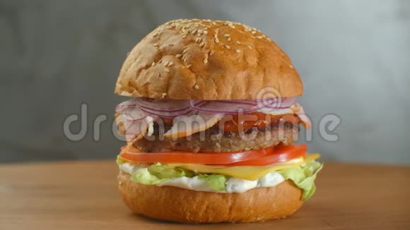 带有牛肉西红柿蘑菇和黄瓜的大汉堡和融化的奶酪在木板上轻轻旋转视频的预览图