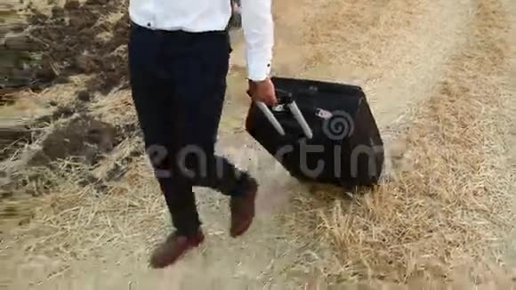 一个穿着商务服的人带着旅行袋来到一片收获的小麦上视频的预览图