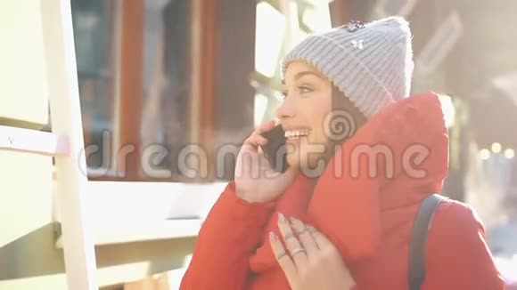 穿着红色冬装的漂亮女人站在满是雪的街道上在一个晴朗的日子里用智能手机聊天视频的预览图