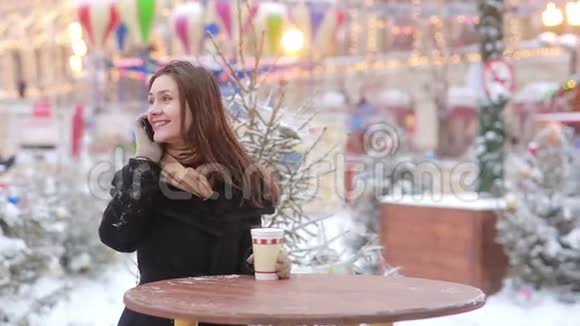 在圣诞集市上美丽的年轻女子打电话喝热茶视频的预览图