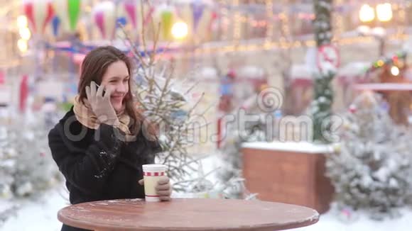 在圣诞集市上美丽的年轻女子打电话喝热茶视频的预览图