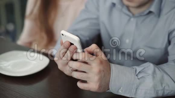 双手特写年轻夫妇在咖啡厅使用智能手机看着展示微笑视频的预览图
