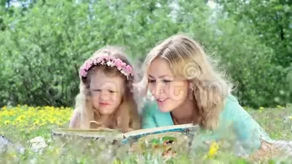 美丽的女人和女孩在户外看书躺在草地上的毯子上视频的预览图
