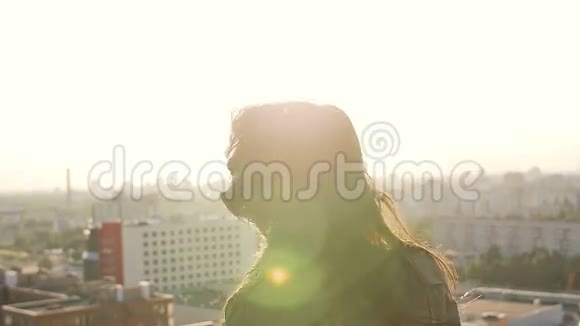 日落时站在屋顶上的年轻女子转过头头发看着相机慢节奏视频的预览图
