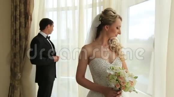 漂亮的年轻新婚夫妇站在窗边婚礼概念视频的预览图