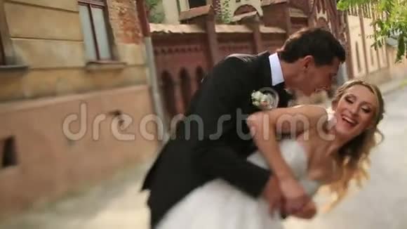快乐的新郎在利沃夫的一个古老的基督教教堂前旋转和亲吻他美丽的金发新娘魅力视频的预览图