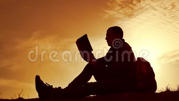 男学生在公园里背着背包看日落人在天空中读书的剪影日落自然温暖视频的预览图