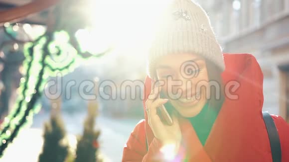 穿着红色冬装的漂亮女人站在满是雪的街道上在一个晴朗的日子里用智能手机聊天视频的预览图