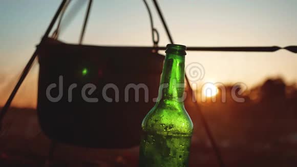点燃一个大锅篝火一瓶啤酒在日落剪影露营特写旅游户外休闲旅游聚会视频的预览图
