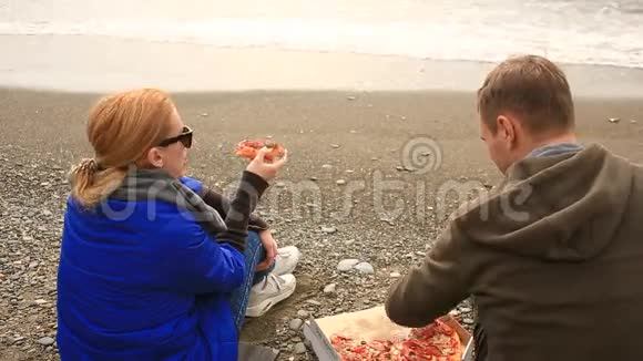 一对夫妇在海边吃披萨天气寒冷在一起视频的预览图