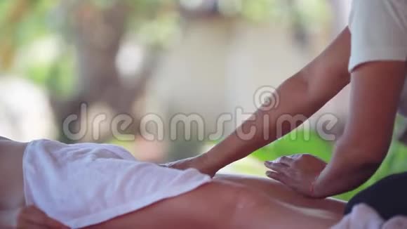 年轻女子躺在热带海滩的水疗沙龙里按摩治疗师做腿部按摩模糊的叶子面包视频的预览图