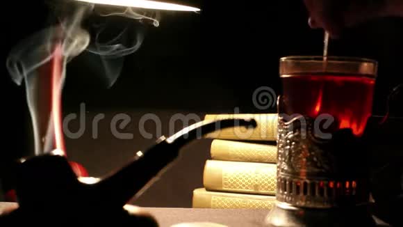 夜读室内一个人把糖混在玻璃杯里的茶里烟斗烟雾缭绕一堆书躺着视频的预览图