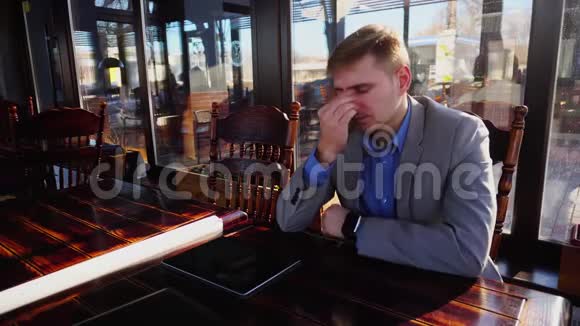 疲惫的年轻教授坐在咖啡馆里桌上放着卷纸智能手机和平板电脑视频的预览图