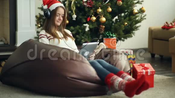 戴着红色圣诞帽和袜子的微笑女孩用垫垫在圣诞树上视频的预览图
