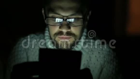 一个戴眼镜穿毛衣在黑暗中拿着平板电脑的家伙视频的预览图