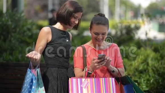 在成功的购物体验后放松年轻女孩带着五颜六色的购物袋在你的智能手机上看到一些东西视频的预览图