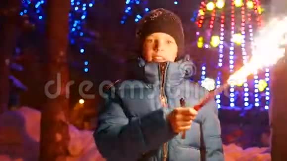 冬天这个孩子在户外拿着火花慢动作在圣诞节的背景灯光和花环视频的预览图