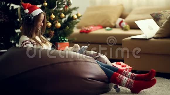 穿着明亮的圣诞袜用垫子听音乐的漂亮女孩视频的预览图