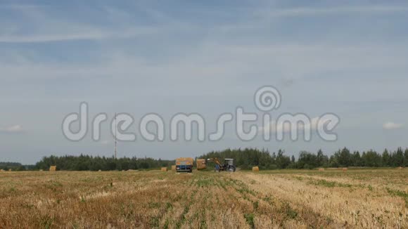 农业拖拉机把一捆捆干草装进农场附近的拖车里视频的预览图