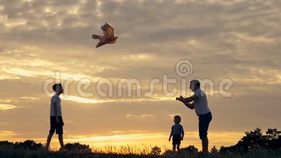 快乐的一家人爸爸和孩子们在草地上奔跑夏天日落时放风筝视频的预览图