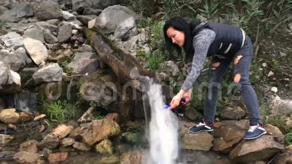 一个女人从山泉中收集水干净的饮用水在山上很高纯净的淡水瀑布视频的预览图