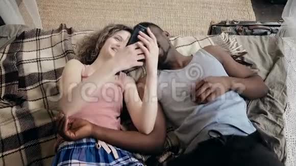 多种族夫妇躺在床上使用智能手机男人和女人在一起快乐男女笑笑视频的预览图