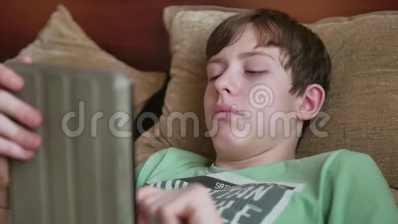 少年躺在室内平板电脑社交媒体十几岁的男孩在床上玩平板电脑游戏视频的预览图
