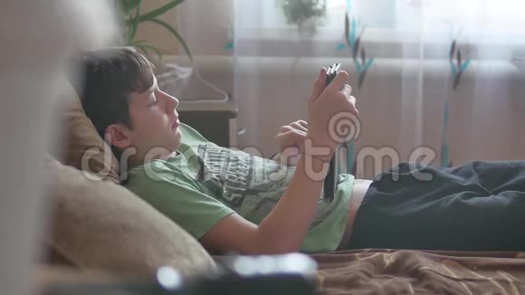 少年室内躺着平板电脑社交媒体十几岁的男孩在床上玩平板电脑游戏视频的预览图