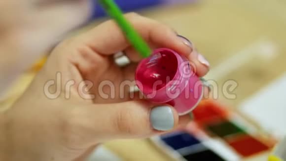 女艺术家的手在画笔上获得红色颜料在特写调色板的颜色在背景视频的预览图